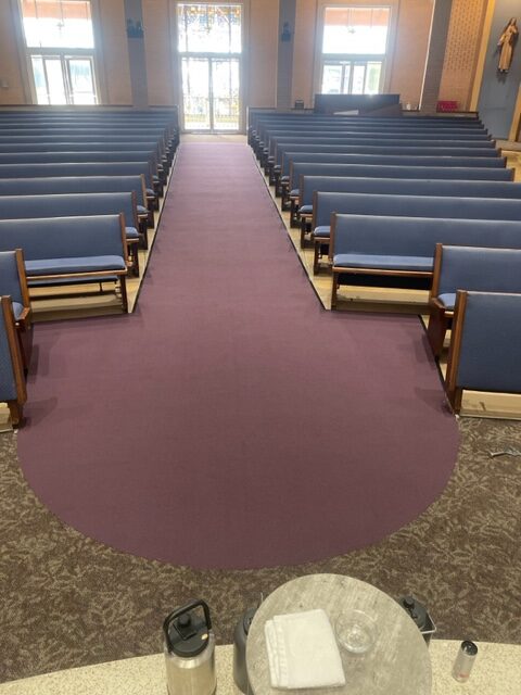 A church with rows of seats and a maroon carpet.
