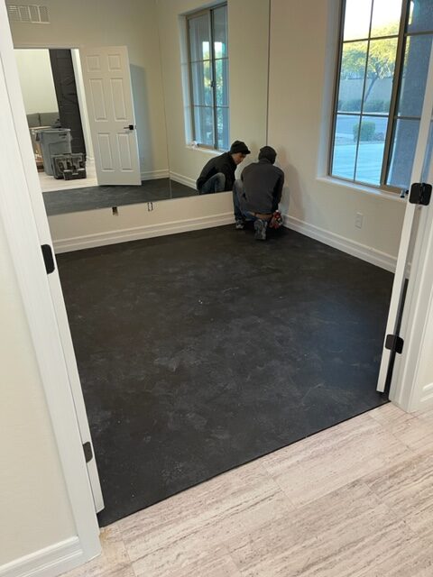 A man is working on a black floor in a room.