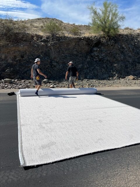 Two men working on a road with a large tarp.