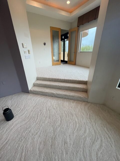 An empty living room with white carpet and stairs.